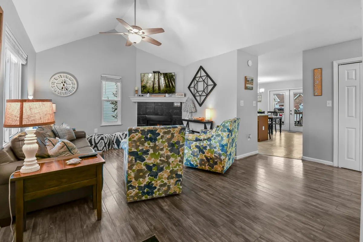 An open-plan view merges the living area’s colorful chairs, cozy sofa, a warm gas log fireplace, and a TV, with glimpses of the adjoining spaces. The design emphasizes seamless flow for group gatherings, and the natural light ensures a cheerful, welcoming mood.