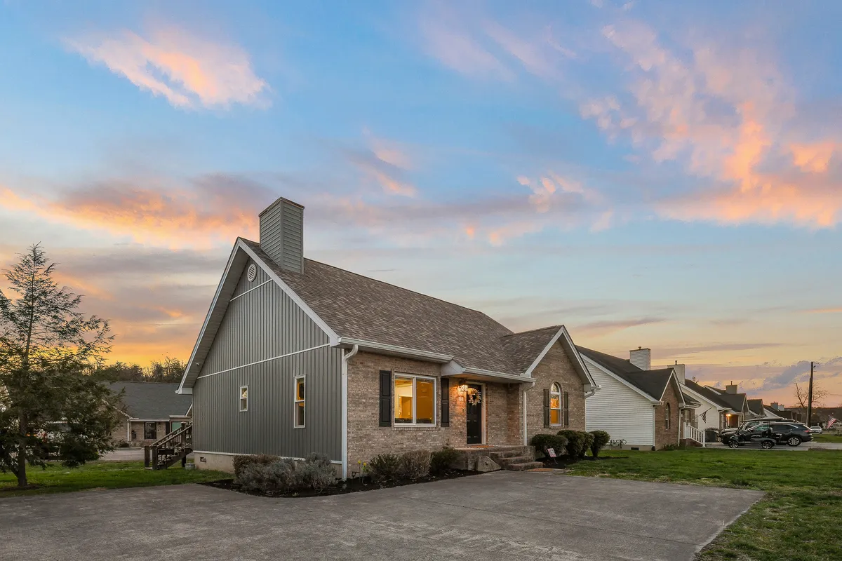 A welcoming exterior view of the house, with its inviting architectural design, warmly lit windows, and a colorful sunset in the background. The scene captures the sense of arrival and the potential for gathering on the porch after a day of adventure.