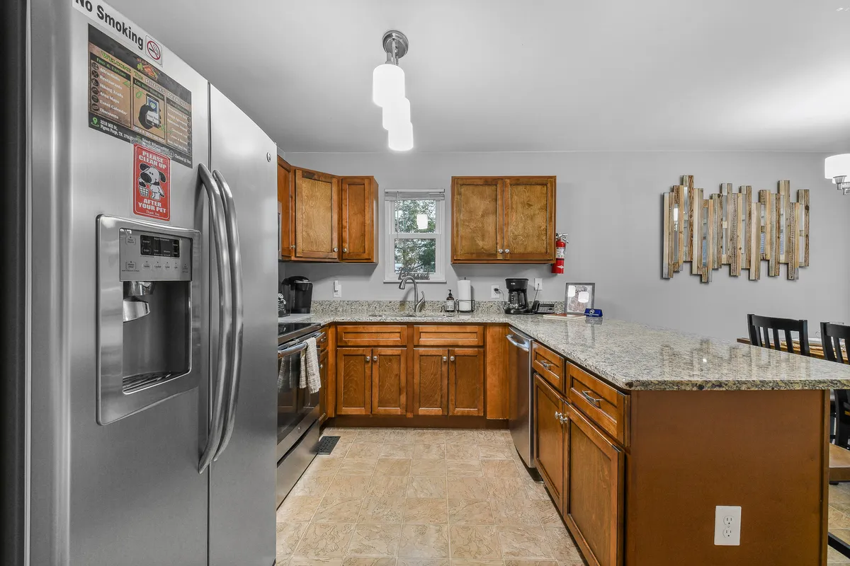 The image captures a contemporary kitchen featuring a stainless steel refrigerator, shining granite countertops, and wooden cabinets. The kitchen island offers ample workspace, and updated appliances are the focal point, reflecting both functionality and style.