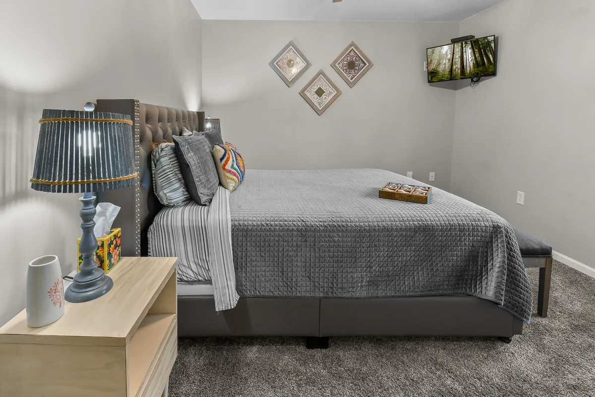 The image displays a calm bedroom with a bed, decorative wall art, lamp, nightstand, and a television mounted in view. The ambiance is restful, and the TV directly references the section's mention of private screen time.