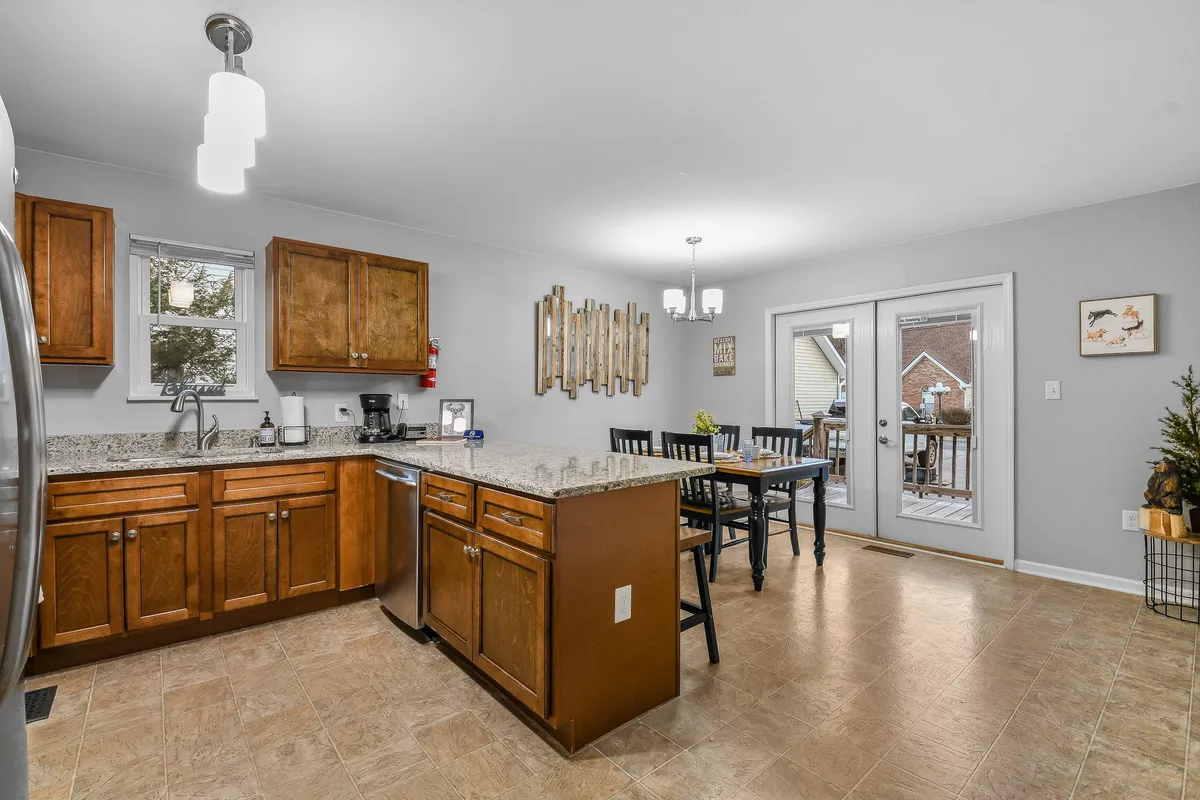 The photo features a cozy dining table set for a meal next to sliding glass doors, with a view of the kitchen’s granite countertops and wood cabinetry in the background. Natural light fills the space, creating a warm, welcoming ambiance for family meals.