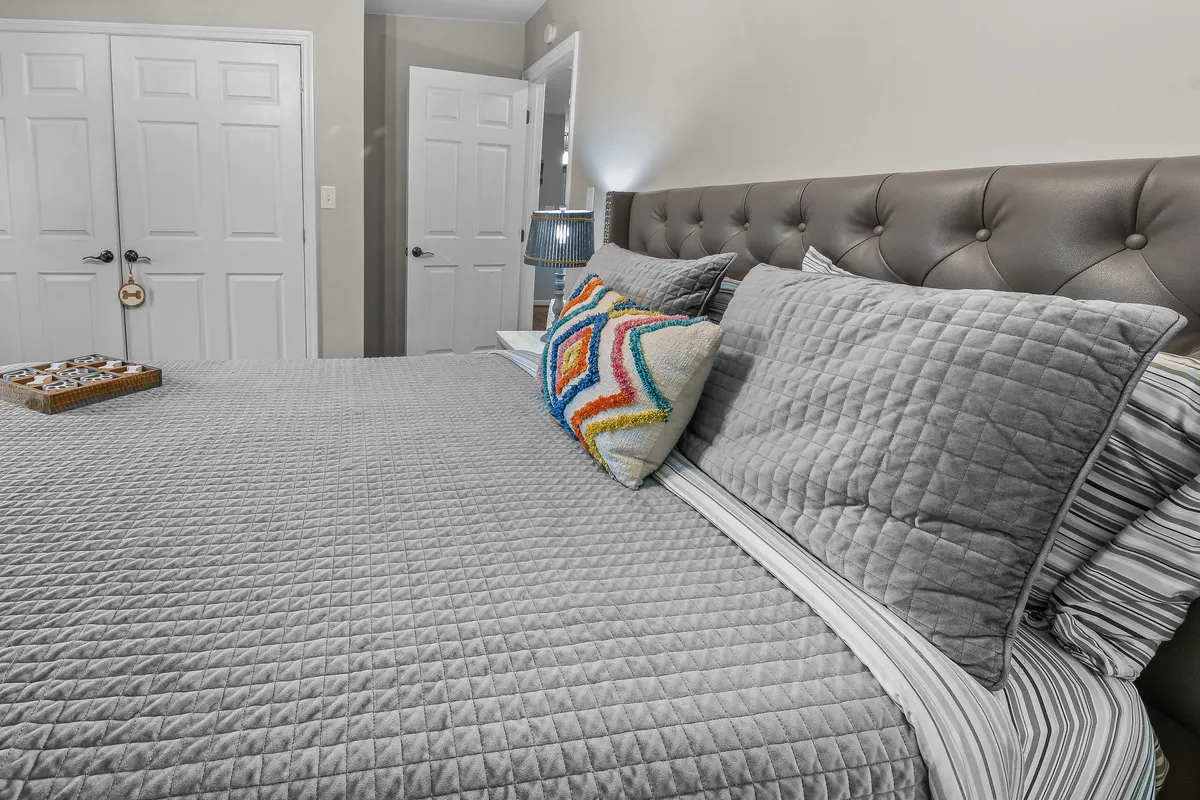 This image features a bed with textured bedding and decorative pillows, a lamp on a nightstand, and a warm, inviting mood. It offers an alternative view of bedroom comfort and highlights the cozy atmosphere.