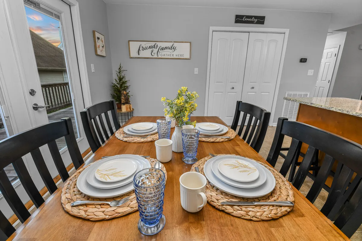A warm, welcoming dining area featuring a dining table set with place settings and a floral centerpiece, accentuated by wall art in the background. The spaciousness and decor invite shared meals and group celebrations.