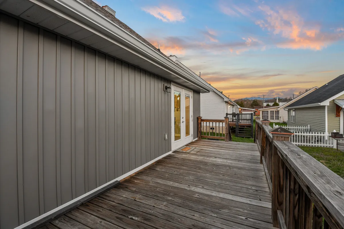 A serene wooden deck attached to the home, with the exterior wall in view, set beneath a beautiful sunset sky. The scene suggests an inviting outdoor space perfect for relaxing or gathering with friends and family after a day of exploring local attractions.