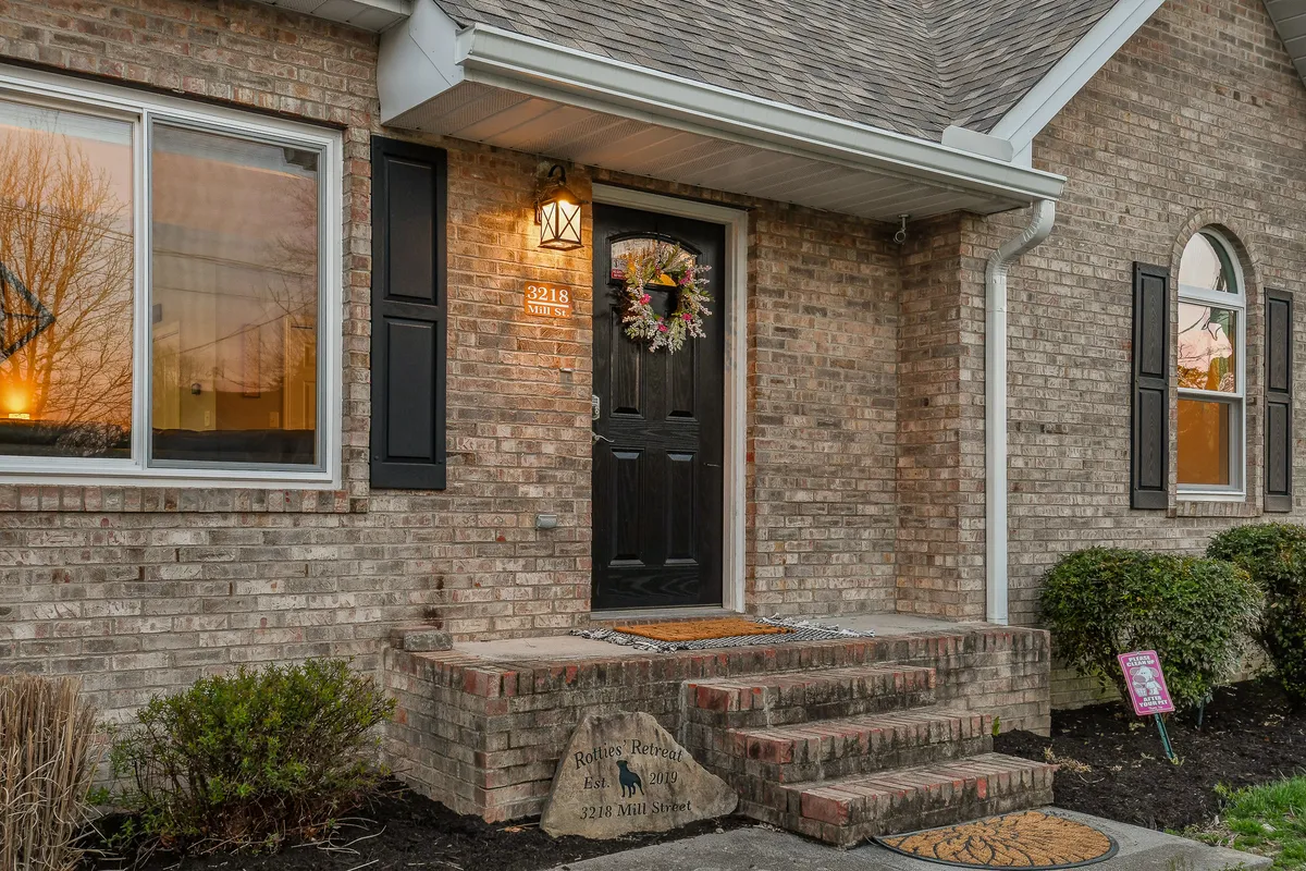 A warmly inviting front entrance, featuring a welcoming door adorned with a wreath, surrounded by tidy landscaping and brick facade. The window reflects the outdoor environment, suggesting a serene neighborhood setting.