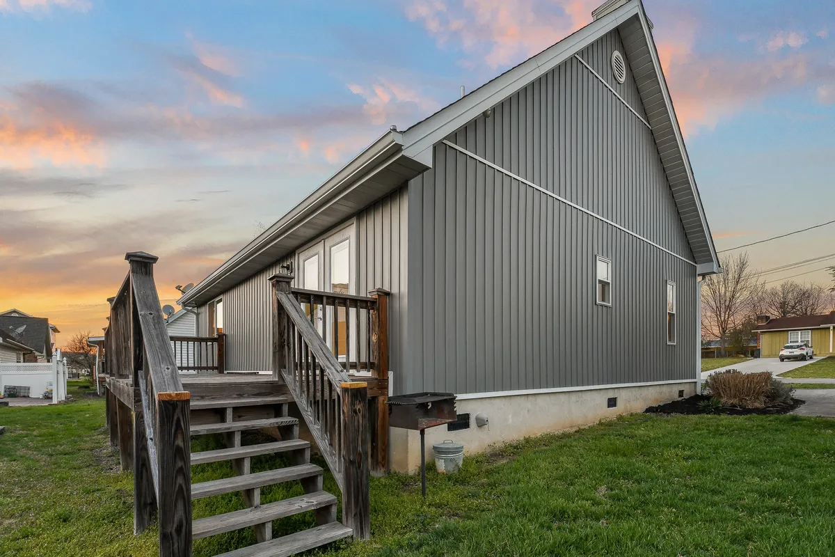 This exterior shot features the wooden steps and gray siding of Rotties' Retreat, set against a picturesque sunset sky. The welcoming porch is visible, inviting guests to relax and enjoy the tranquil outdoor setting.