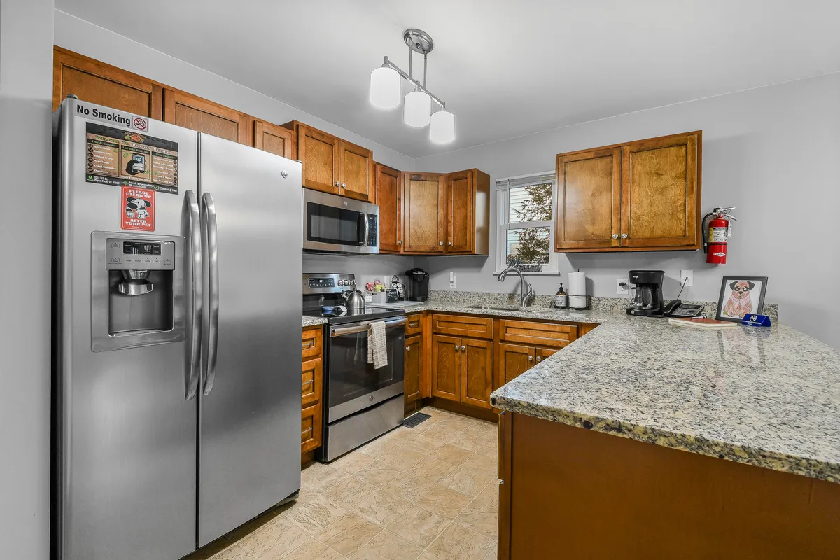 A modern kitchen with a stainless steel refrigerator, granite countertop, wood cabinetry, and a kitchen island. The layout is ideal for meal prep and socializing, reflecting the home’s suitability for group stays.