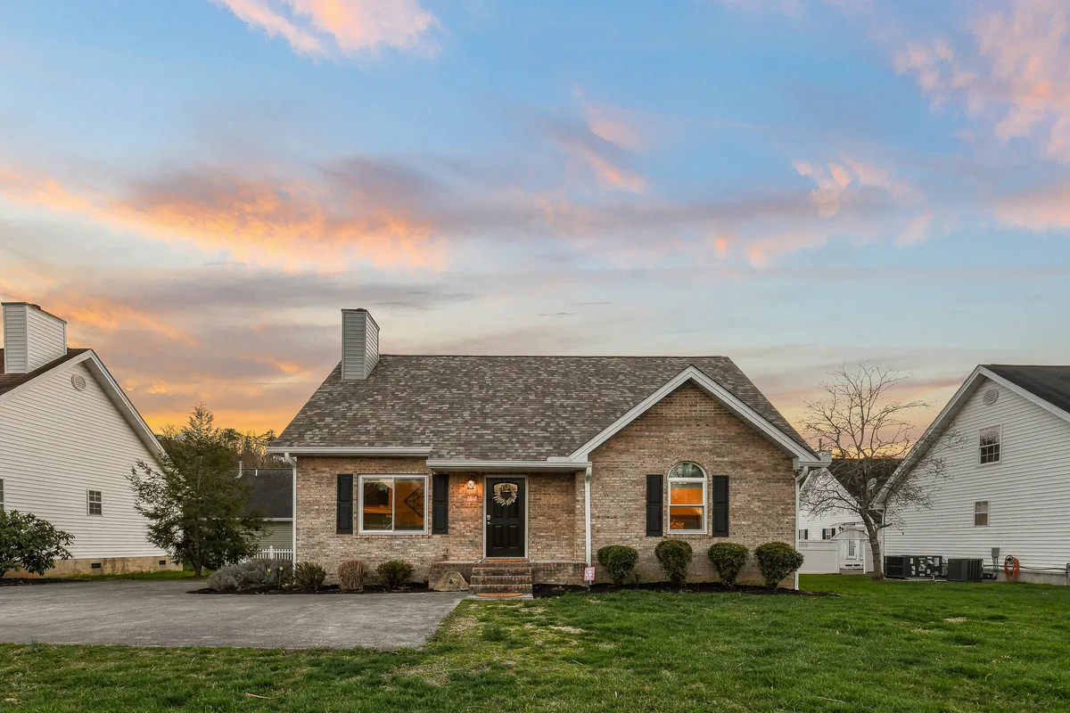 A wide exterior shot of the home’s entrance, showcasing the front door, landscaped bushes, roofline, and windows. The composition suggests a space ideal for family gatherings and outdoor activities like grilling or relaxing in green areas.