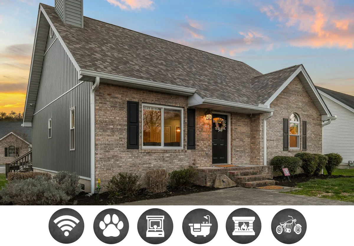The image shows the front exterior of a charming, single-family house in Pigeon Forge, Tennessee. The inviting front door and large windows are framed by lush landscaping, and a spacious porch offers the perfect spot to relax and watch sunsets. The overall scene is warm and welcoming, perfect for family gatherings, outdoor play, or unwinding on summer evenings.